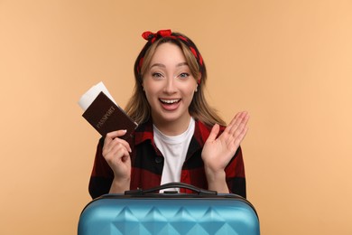 Emotional young woman with passport, ticket and suitcase on beige background