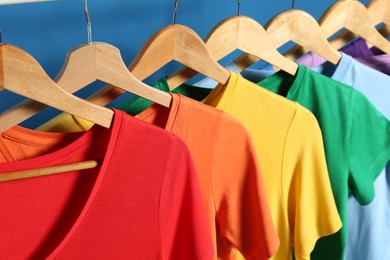 Photo of Bright clothes on wooden hangers against blue background, closeup. Rainbow colors