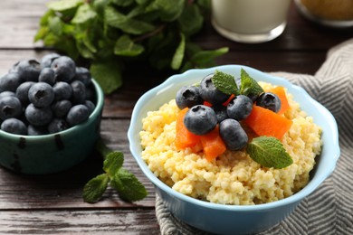 Photo of Tasty millet porridge with blueberries, pumpkin and mint in bowl on wooden table, closeup