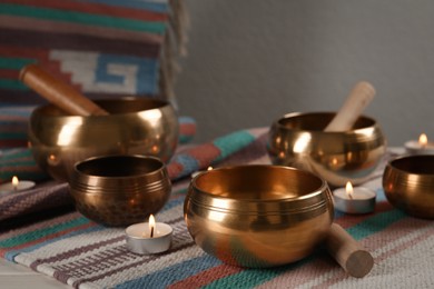 Photo of Tibetan singing bowls with mallets, burning candles and colorful fabric on white table