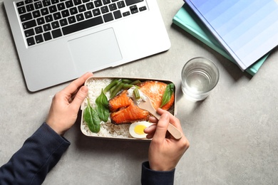 Photo of Woman eating natural protein food from container at office table, top view