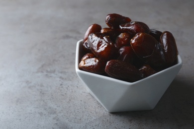 Photo of Bowl with sweet dates on grey background, space for text. Dried fruit as healthy snack