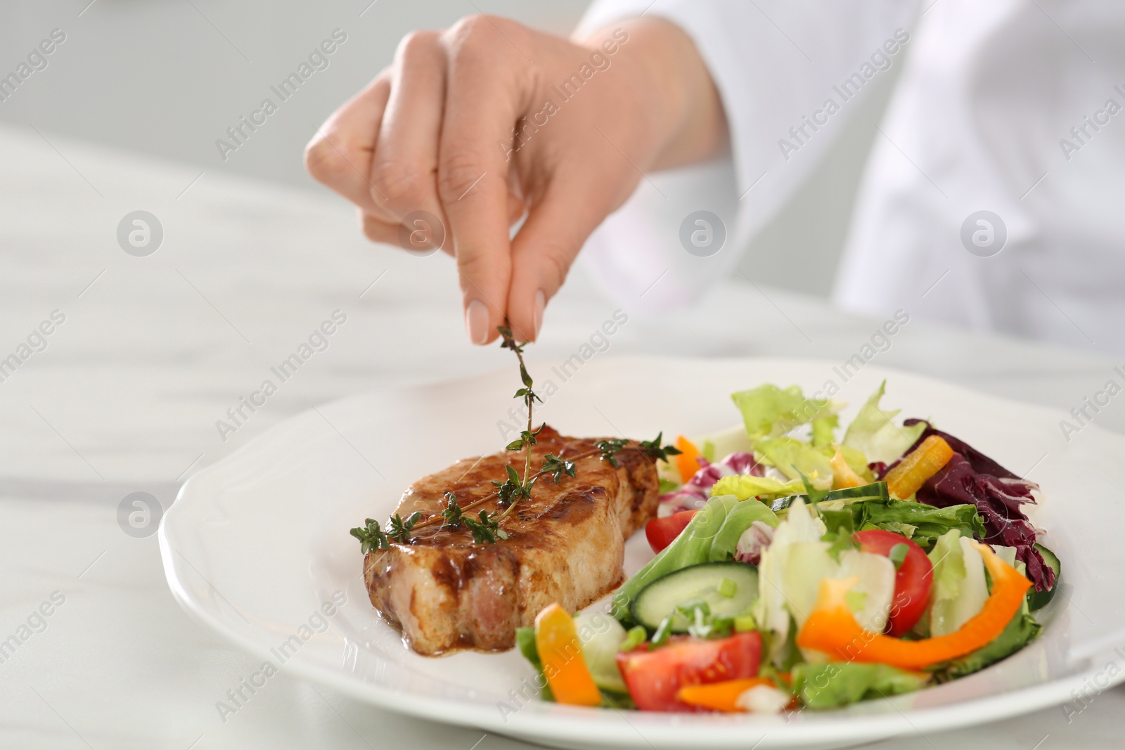 Photo of Professional chef decorating delicious dish with thyme at marble table, closeup