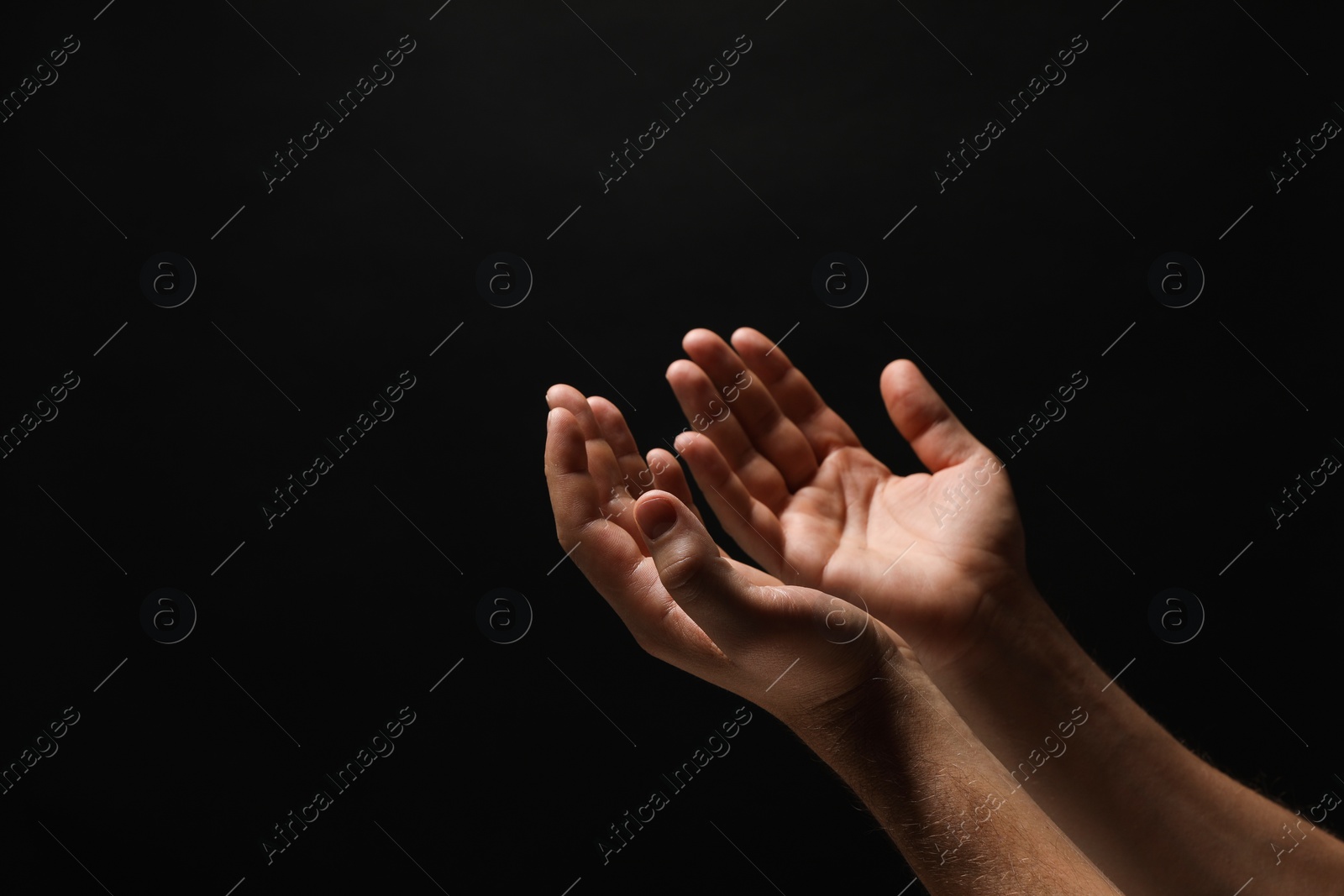 Photo of Religion. Man with open palms praying on black background, closeup. Space for text