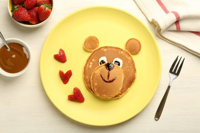 Photo of Creative serving for kids. Plate with strawberries, cute bear made of pancakes on light wooden table, flat lay