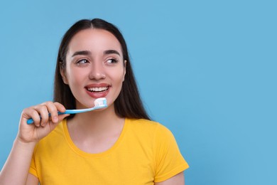 Happy young woman holding plastic toothbrush with toothpaste on light blue background, space for text