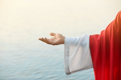 Jesus Christ reaching out his hand near water outdoors, closeup