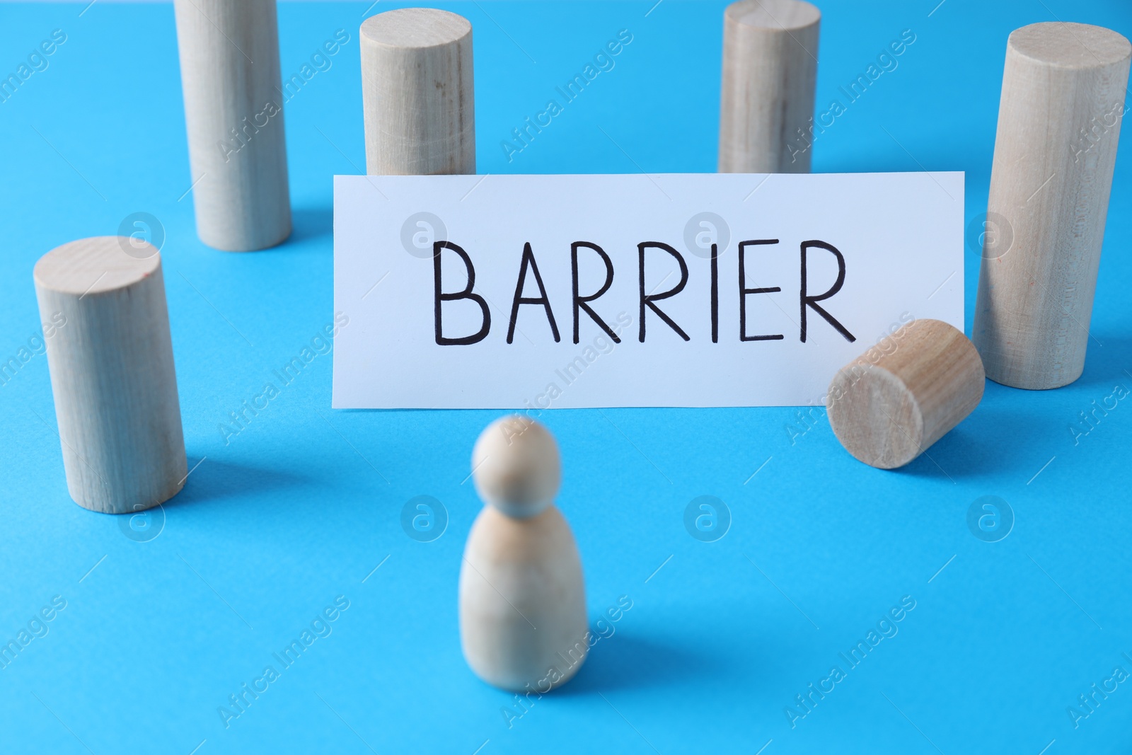 Photo of Blocks as barrier blocking way for wooden human figure on light blue background. Development through obstacles overcoming