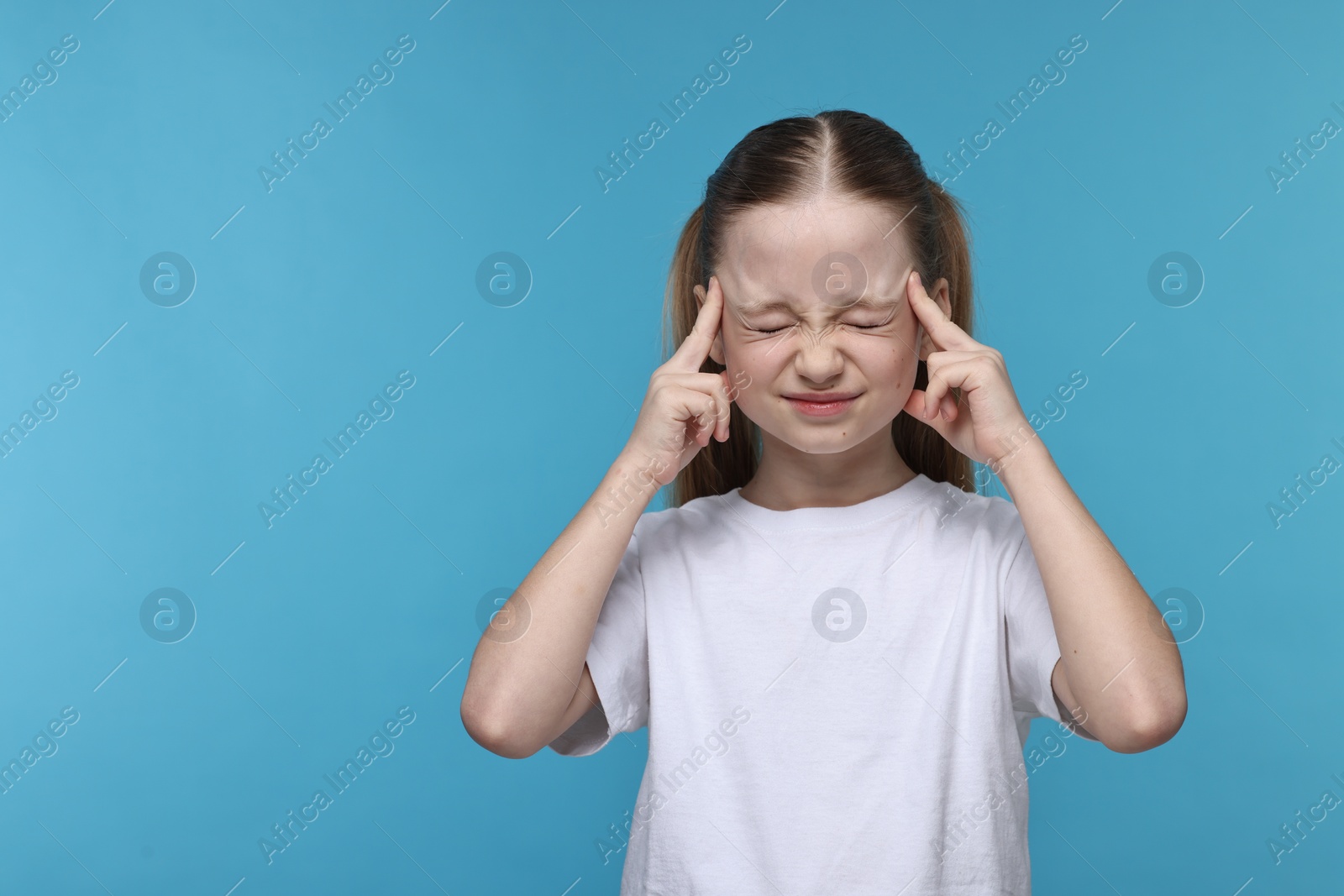 Photo of Little girl suffering from headache on light blue background. Space for text