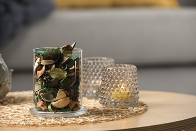 Photo of Glass jar with aromatic potpourri of dried flowers and burning candles on wooden table indoors