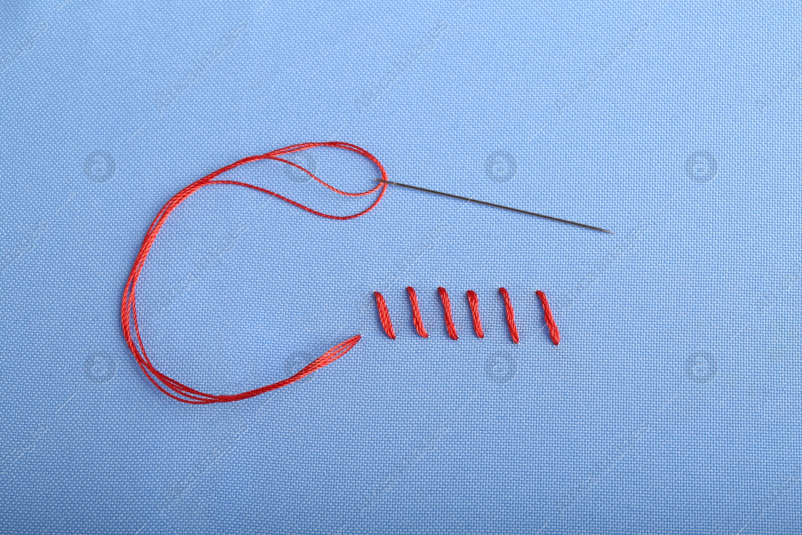 Photo of Sewing needle with thread and stitches on blue cloth, top view