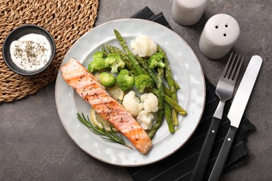 Photo of Healthy meal. Piece of grilled salmon, vegetables, asparagus and rosemary served with sauce on grey textured table, flat lay