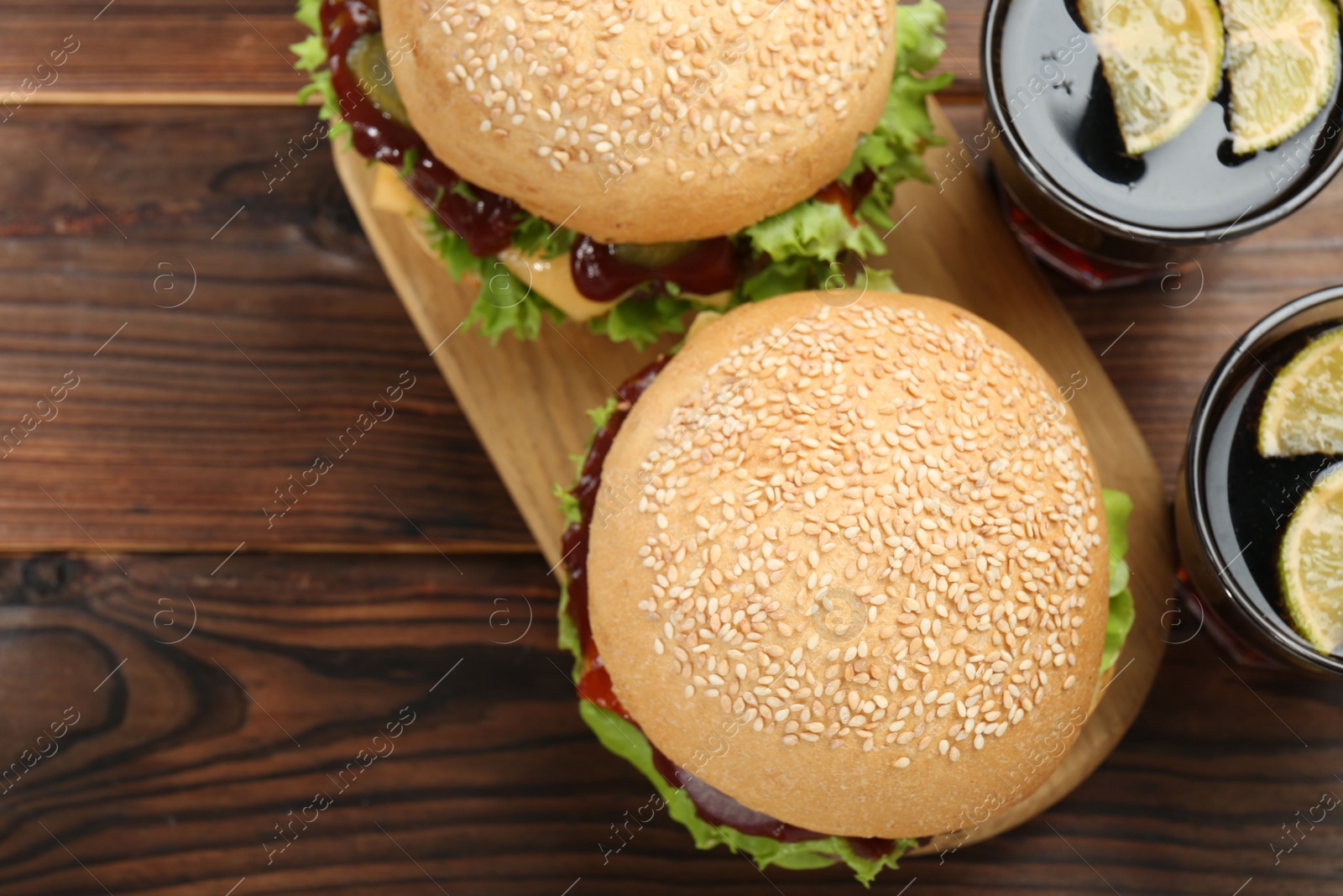 Photo of Delicious cheeseburgers and drinks on wooden table, top view. Space for text