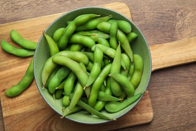 Photo of Bowl with green edamame beans in pods on wooden table, top view