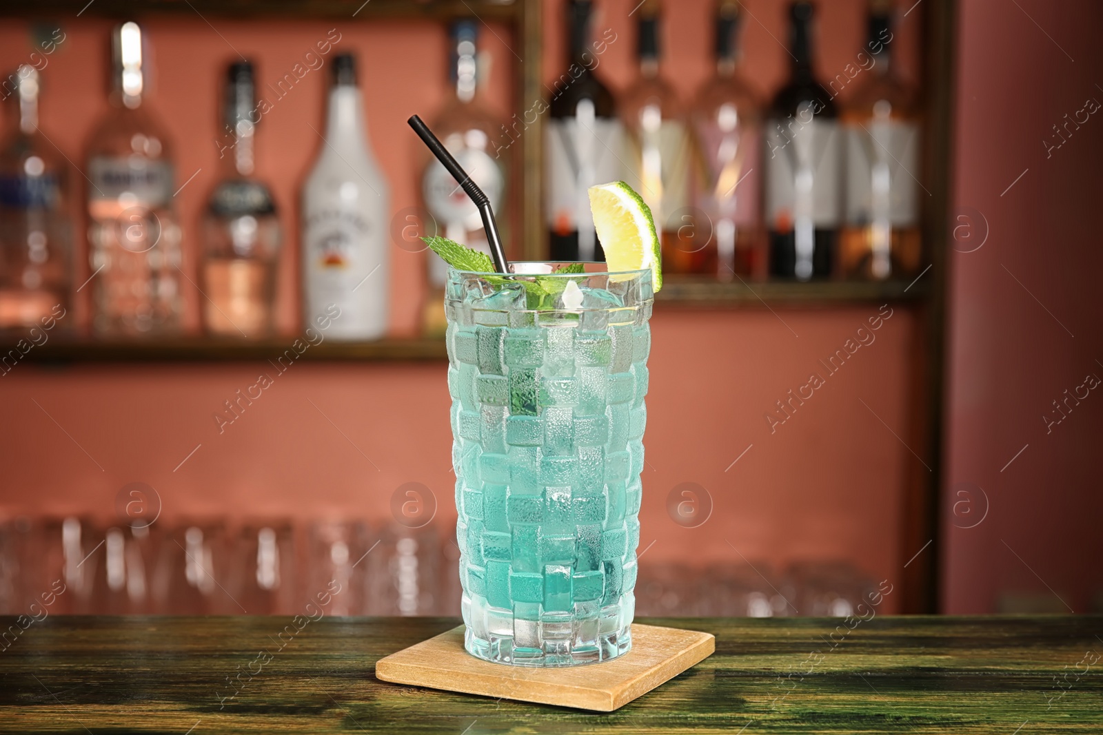 Photo of Glass with delicious cocktail and ice cubes on counter in bar