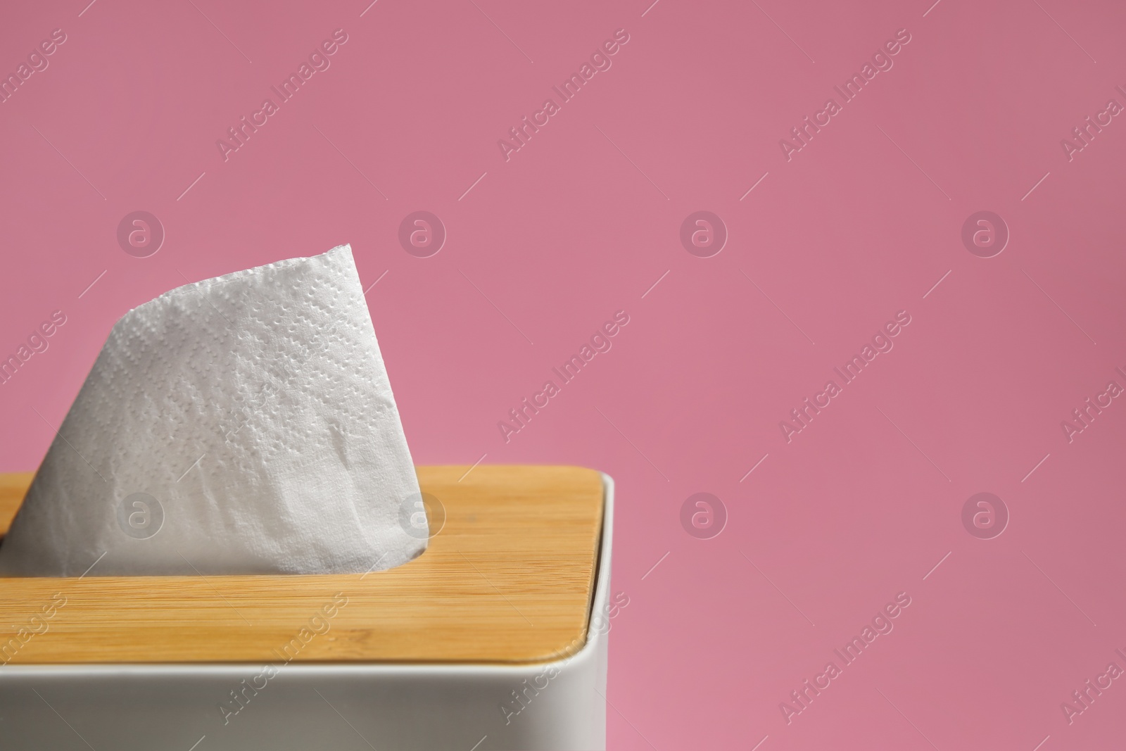 Photo of Holder with paper tissues on pink background, closeup. Space for text