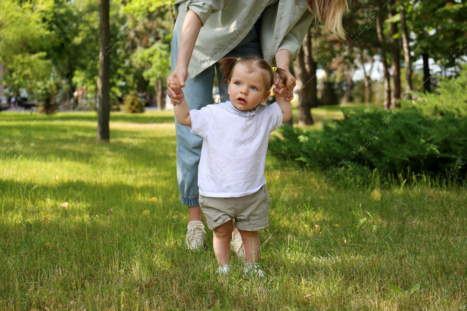 Photo of Mother supporting daughter while she learning to walk in park, closeup