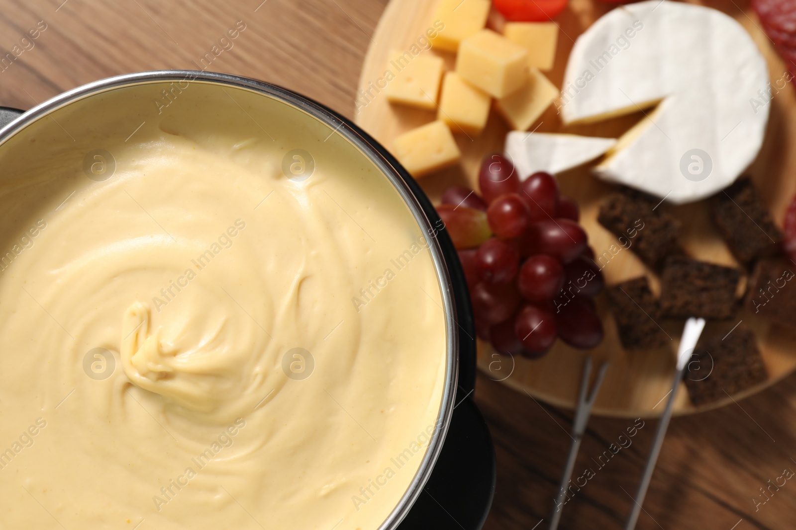 Photo of Fondue with tasty melted cheese, forks and different snacks on wooden table, top view