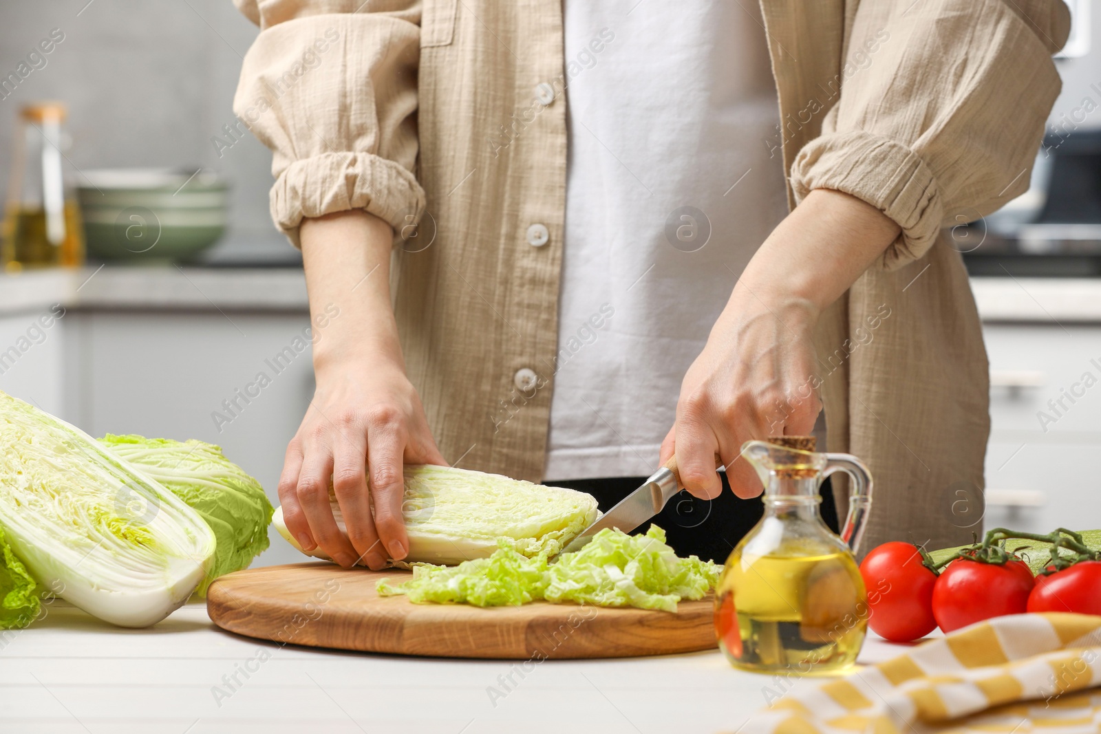 Photo of Woman cutting fresh chinese cabbage at white wooden table in kitchen, closeup