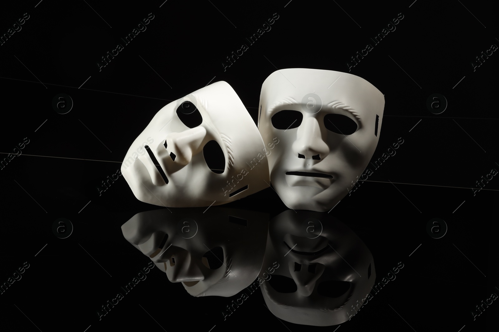 Photo of Plastic face masks on black mirror surface. Theatrical performance