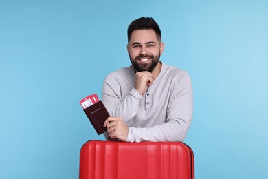 Photo of Smiling man with passport, tickets and suitcase on light blue background