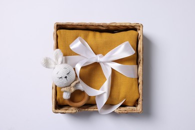 Photo of Baby accessory. Rattle and child`s clothes in wicker box on white background, top view