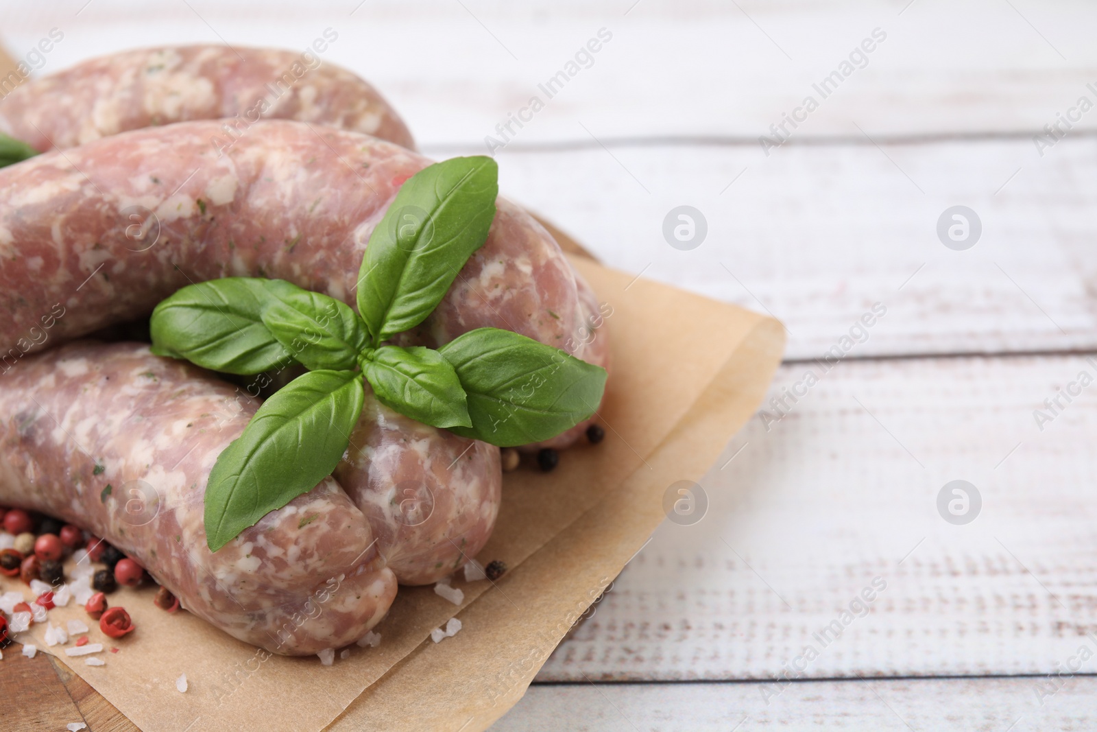 Photo of Raw homemade sausages and different spices on white wooden table, closeup. Space for text