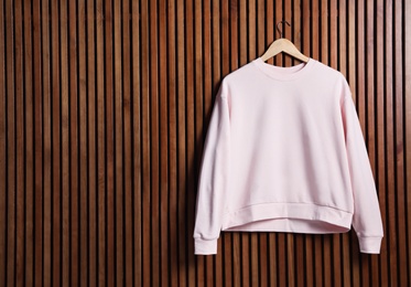 Photo of Hanger with new sweater on wooden wall, mock up for design