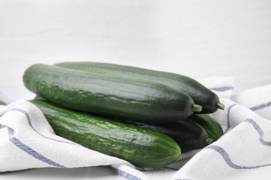 Fresh cucumbers and cloth on white table, closeup