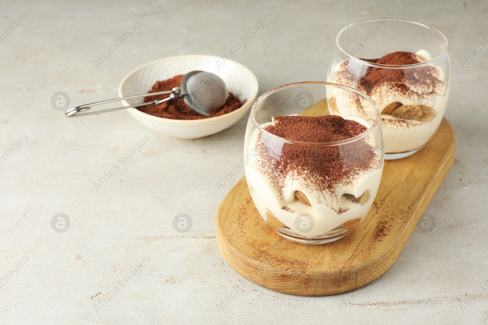 Photo of Delicious tiramisu in glasses on light table, Space for text