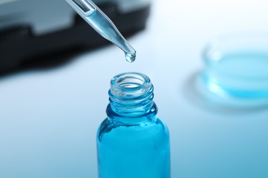 Dripping liquid from pipette into glass bottle on blurred background, closeup