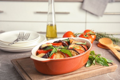 Photo of Baked eggplant with tomatoes, cheese and basil in dishware on table