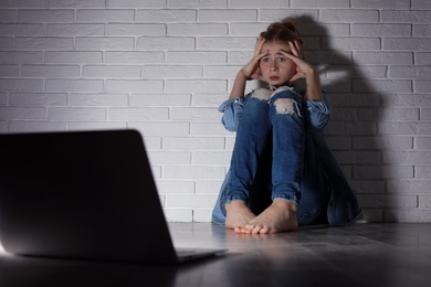 Photo of Scared teenage girl with laptop on floor in dark room. Danger of internet