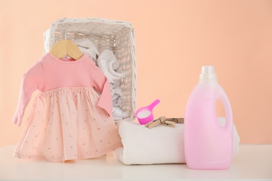 Photo of Detergent and children's clothes on white table near pink wall