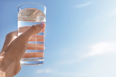 Photo of Woman holding glass of refreshing drink against blue sky on hot summer day, closeup. Space for text