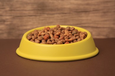 Photo of Dry pet food in feeding bowl on brown background, closeup