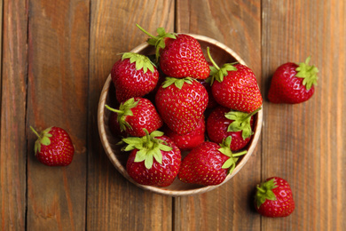 Photo of Delicious ripe strawberries in bowl on wooden table, flat lay