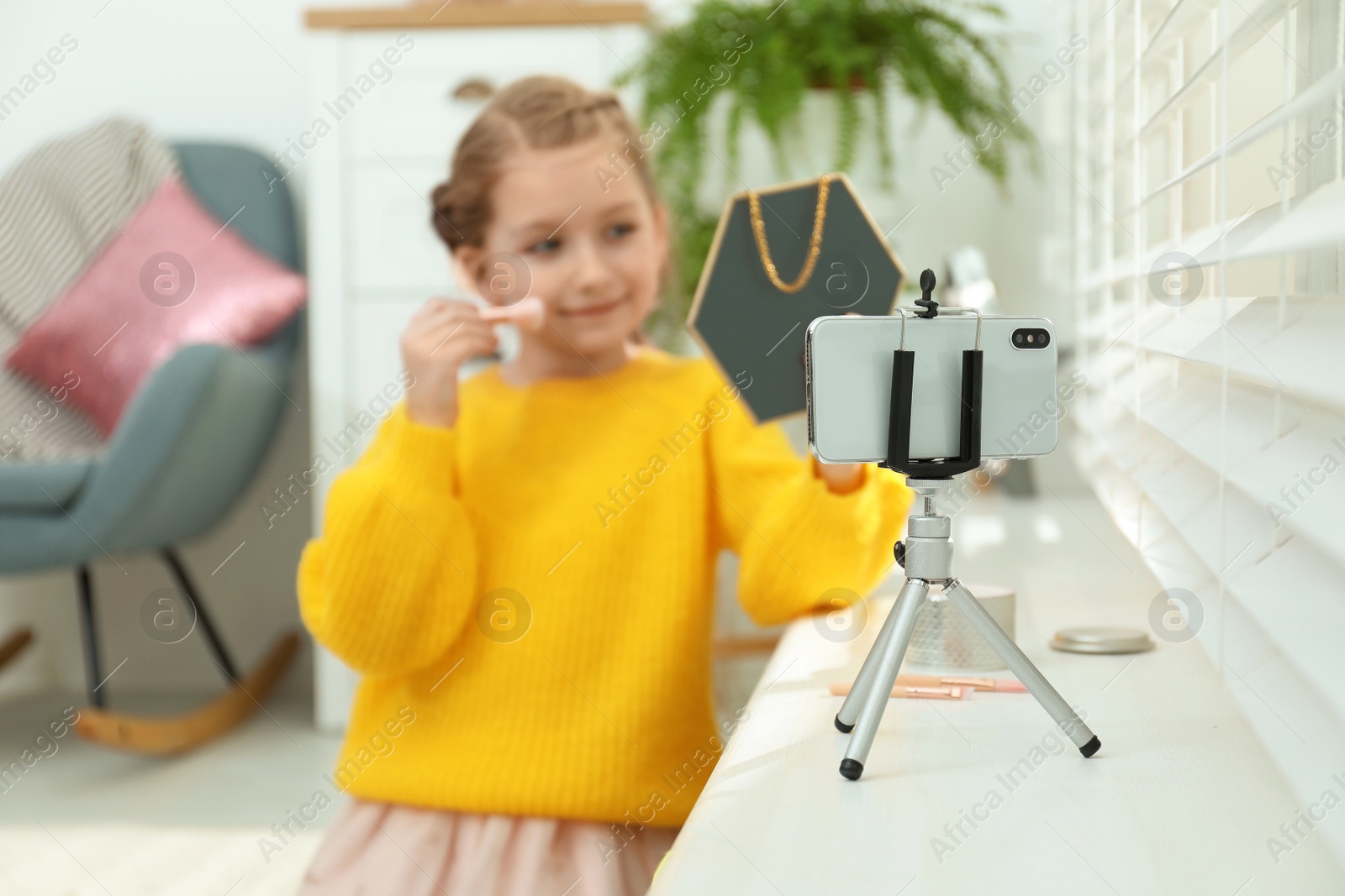 Photo of Cute little blogger with cosmetics recording video at home, focus on phone