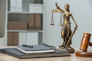 Photo of Figure of Lady Justice, gavel and notebooks on wooden table indoors, space for text. Symbol of fair treatment under law