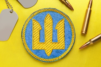 Photo of Flat lay composition with Ukrainian army chevron, military ID tags and bullets on yellow background