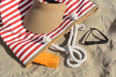 Photo of Stylish striped bag with beach accessories on sand, closeup