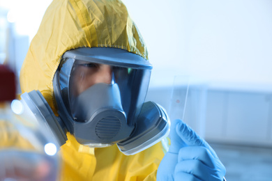 Photo of Scientist in chemical protective suit with microscope slide at laboratory. Virus research