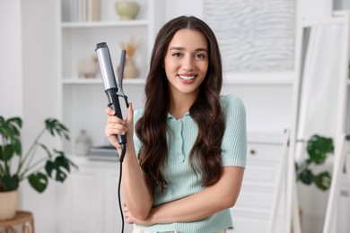 Photo of Happy woman with curling hair iron at home