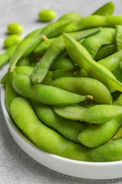 Photo of Plate with green edamame beans in pods on light grey table, closeup