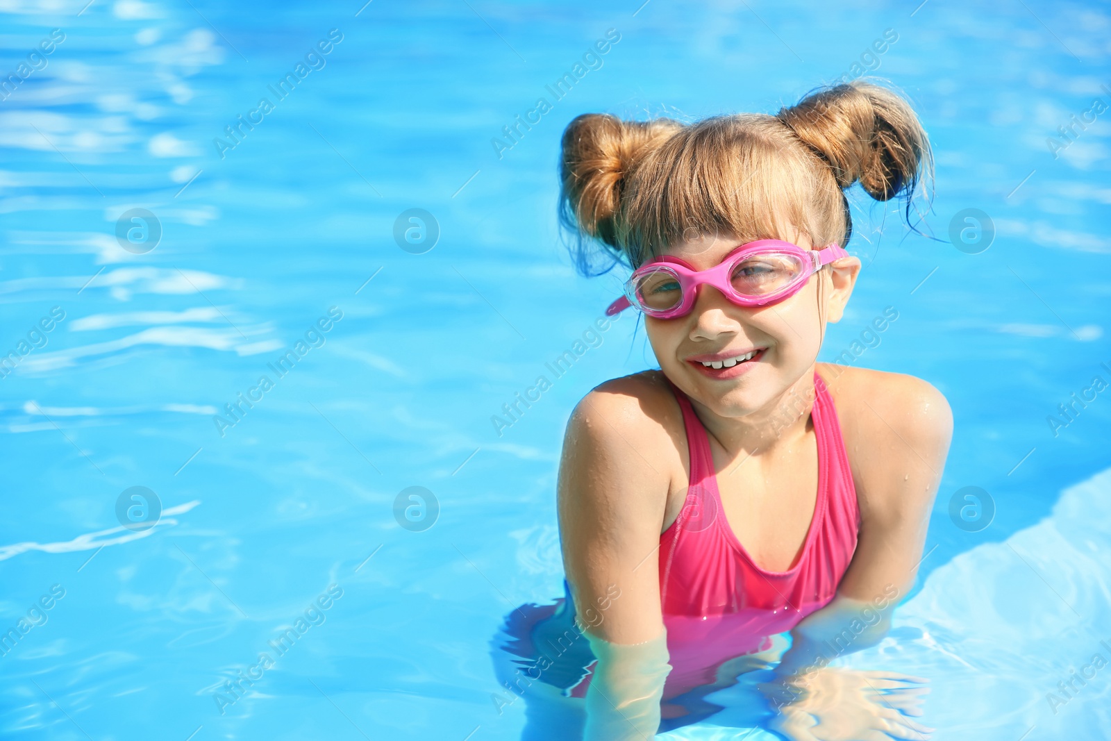 Photo of Happy girl wearing goggles in swimming pool. Space for text