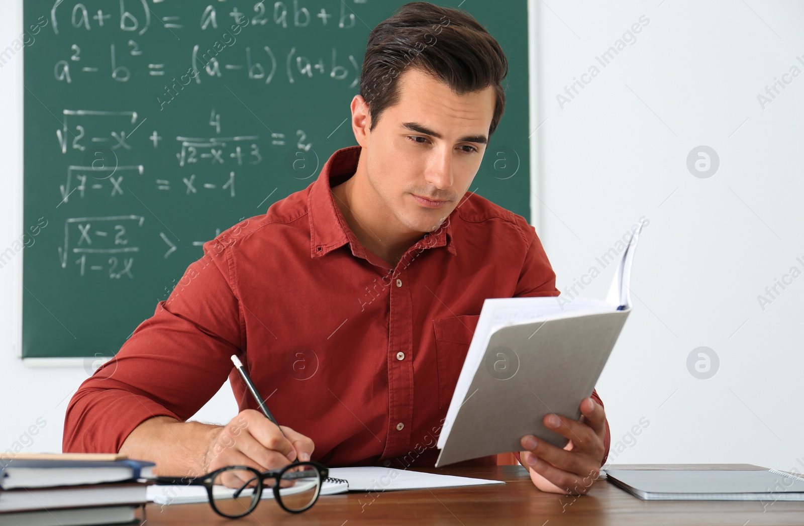 Photo of Young teacher working at table in classroom