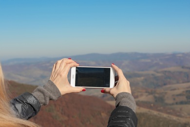 Photo of Woman taking photo of beautiful mountain landscape with smartphone