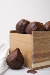 Wooden crate with fresh salak fruits on white table, closeup