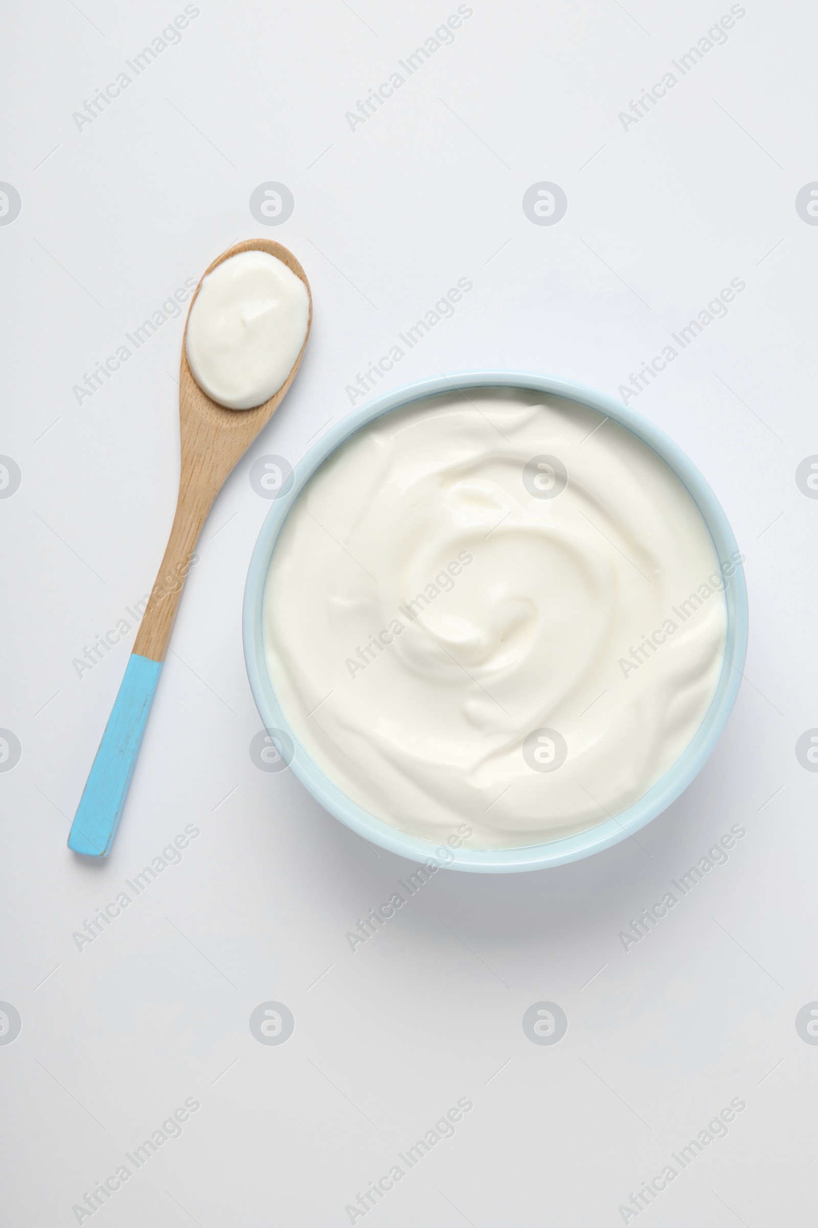 Photo of Bowl of sour cream and wooden spoon on white background, top view