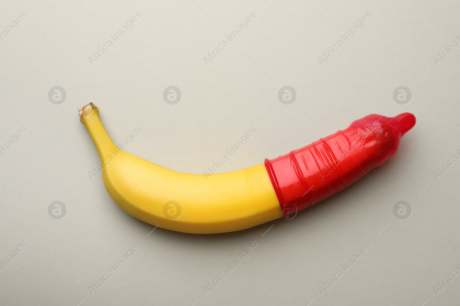 Photo of Banana with condom on light grey background, top view. Safe sex concept